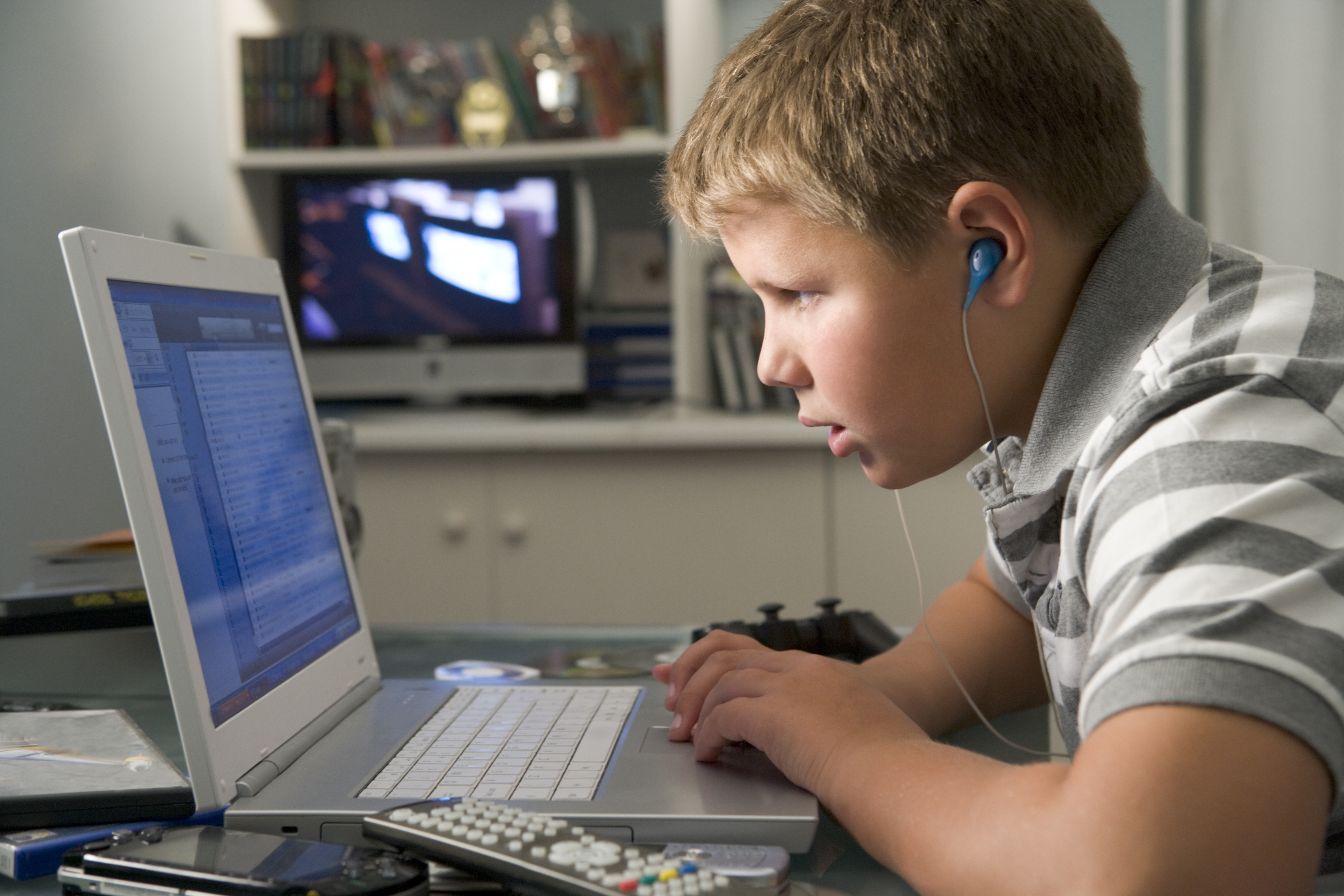 Young boy in bedroom using a laptop computer and listening to headphones