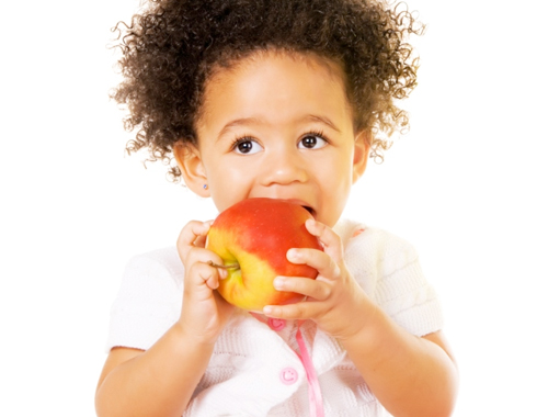 A small baby looks up as she bites an apple.