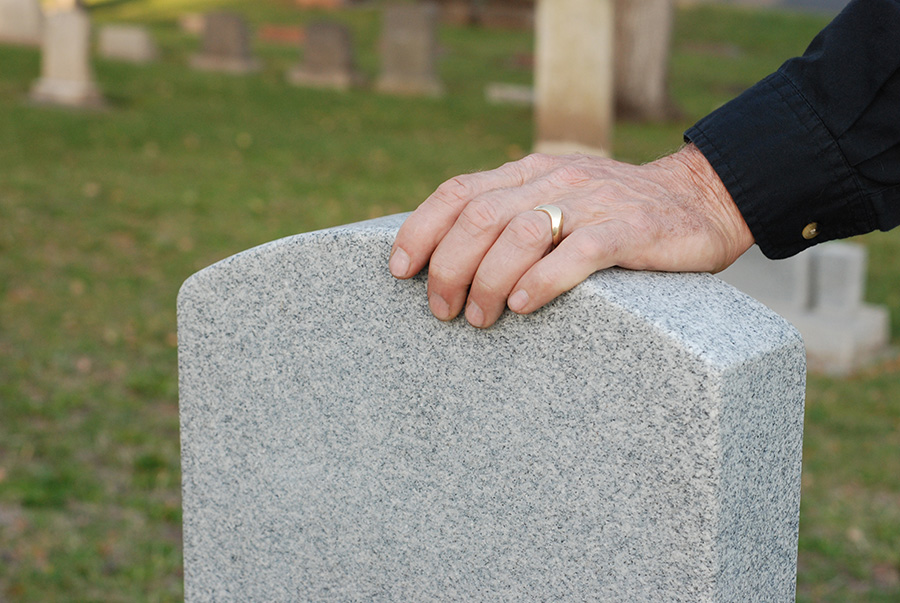 A person’s hand on a tombstone in a cemetery.