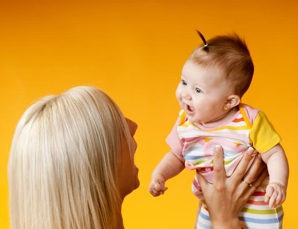 A mother lifts her baby with two hands and they smile at each other. 