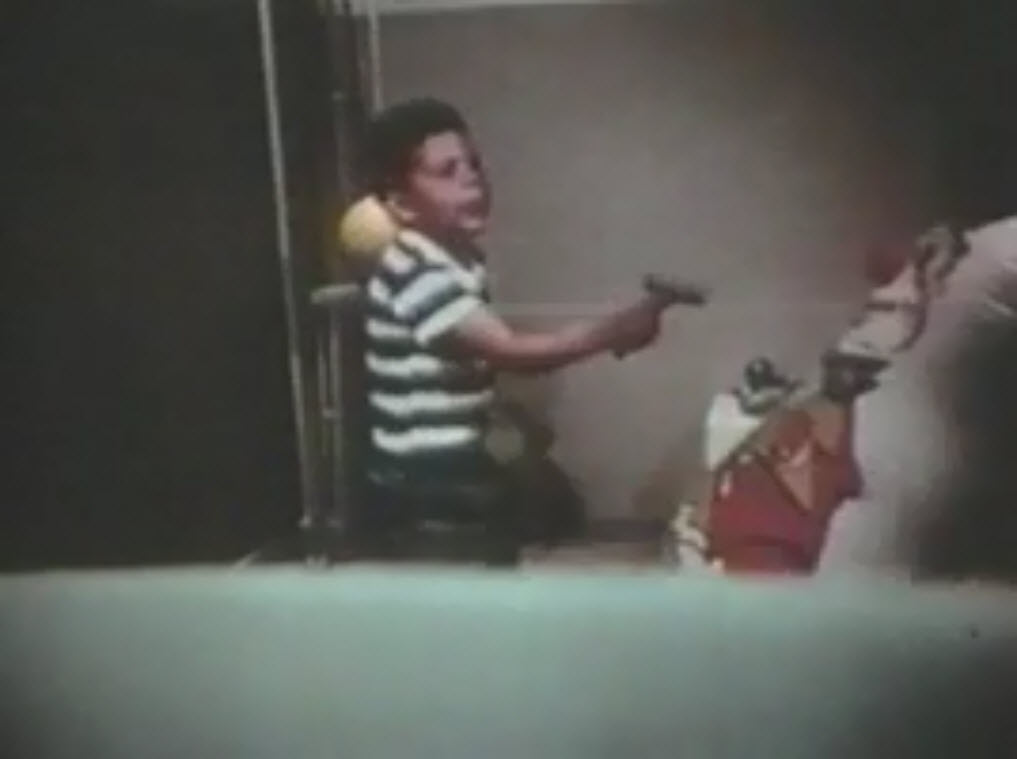 The image is a still photo of a video showing a boy holding a hammer and standing in front of a Bobo doll.