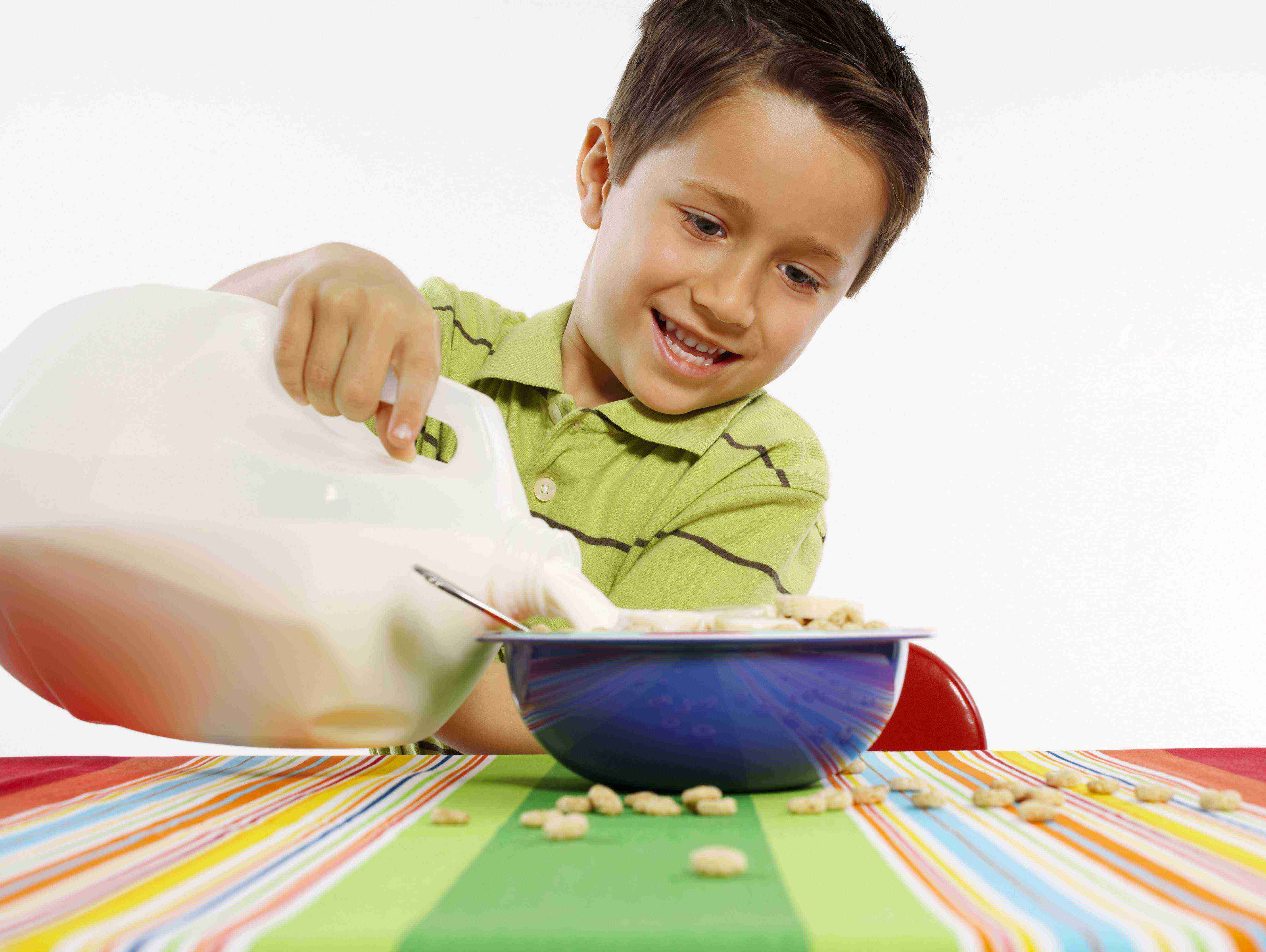 A young boy is pouring milk into a cereal bowl