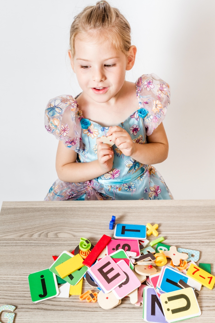 Blonde little girl playing with colorful letters on wooden table