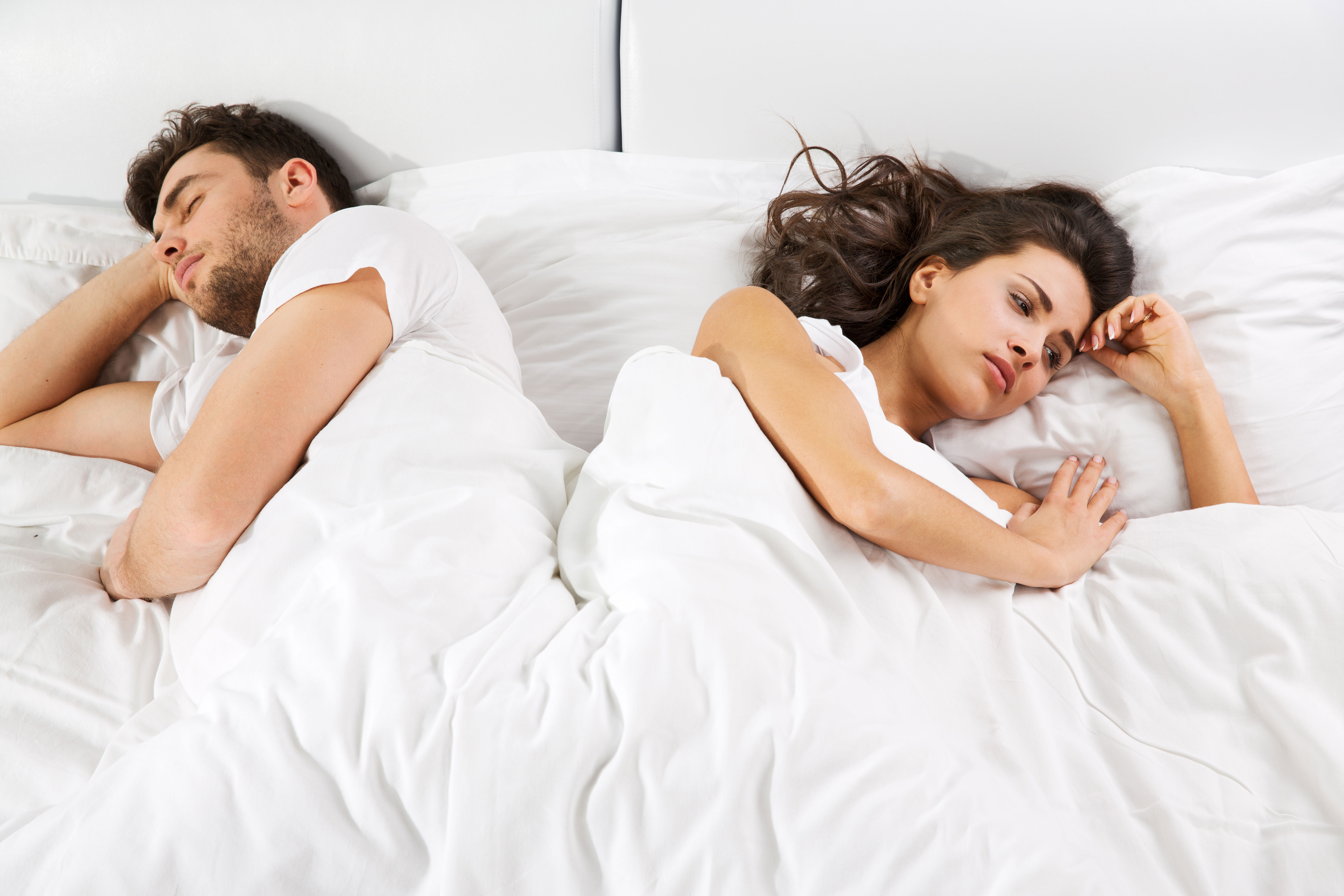 Photo: male-female couple in bed, facing opposite directions, suggesting failed intimacy
