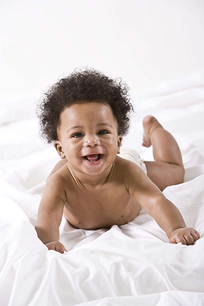 Happy adorable African American baby crawling, on white blanket