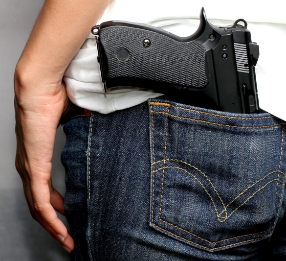 A person with a pistol in the back pocket of his denim jeans.