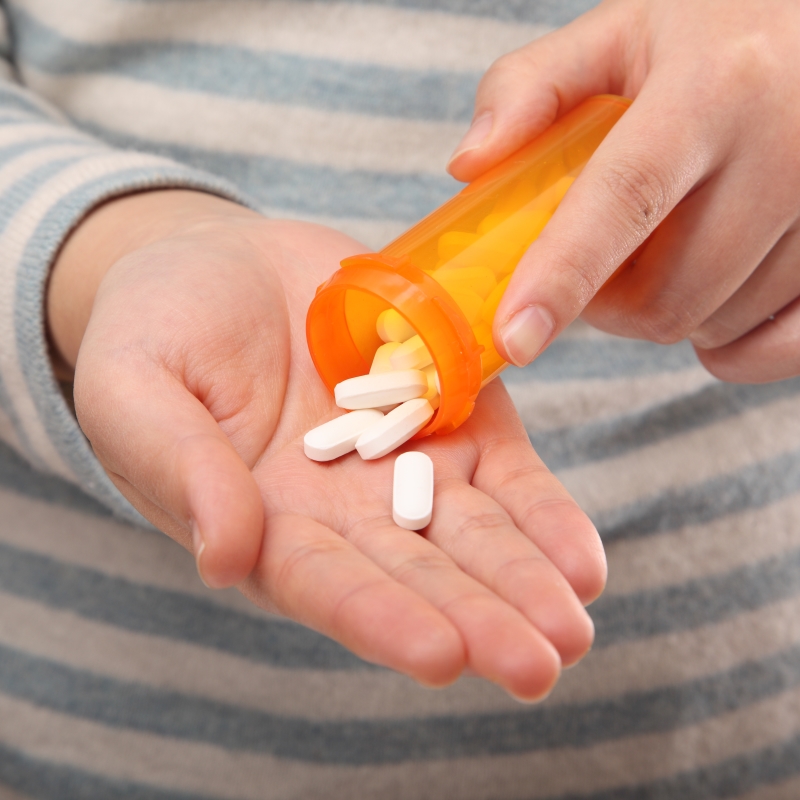 A young person holds an amber-colored medicine bottle in one hand and drops few pills into the palm of other hand.