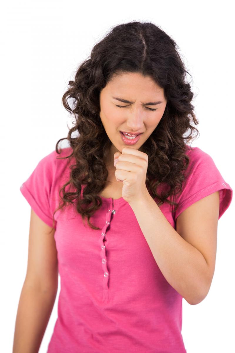 A young girl in a pink shirt sneezes.