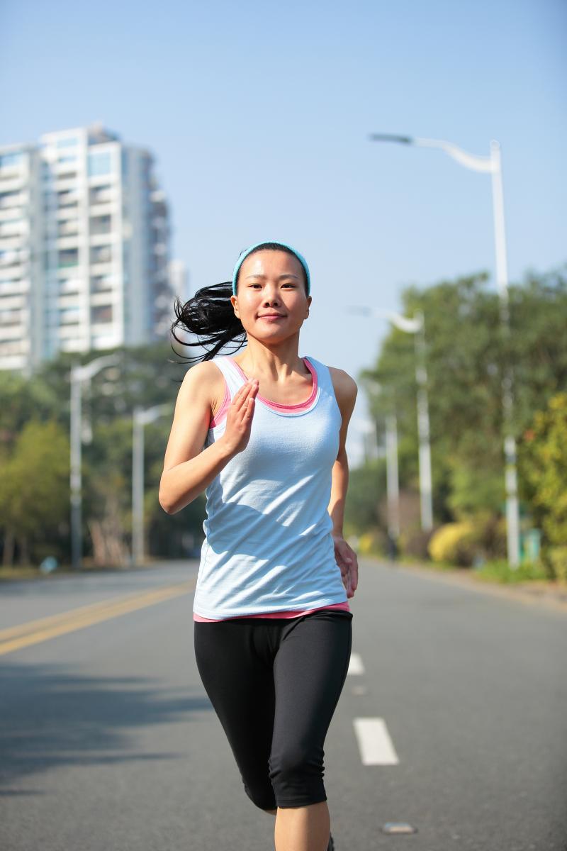 A young asian woman in sports wear runs in to the middle of an empty city road.