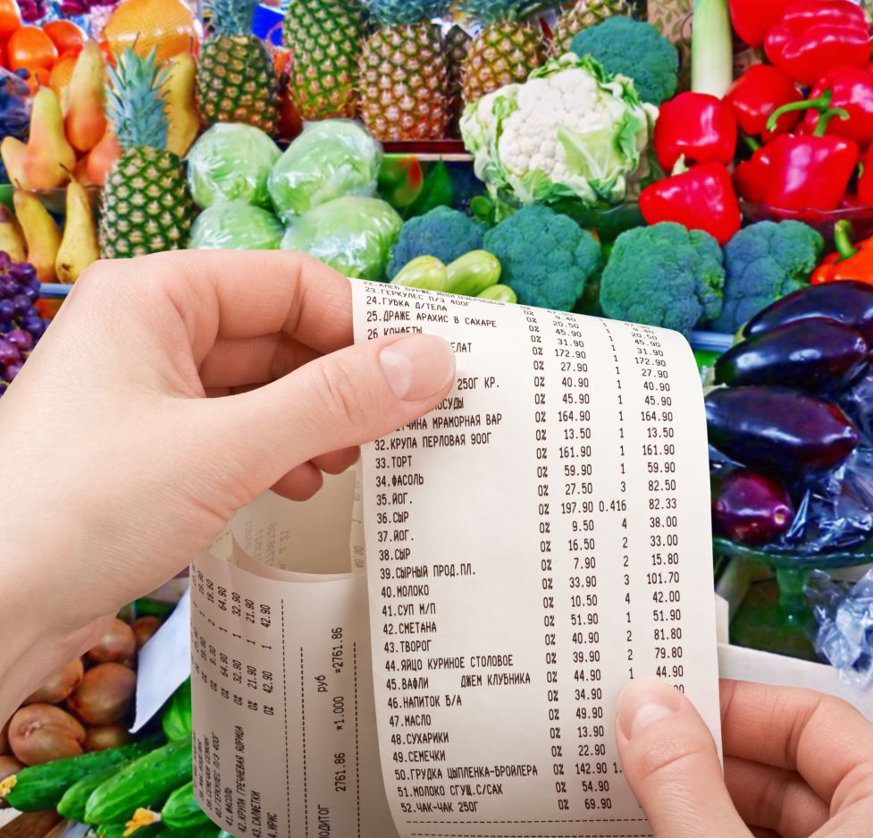 Hand holding grocery store receipt with colorful produce in the background.