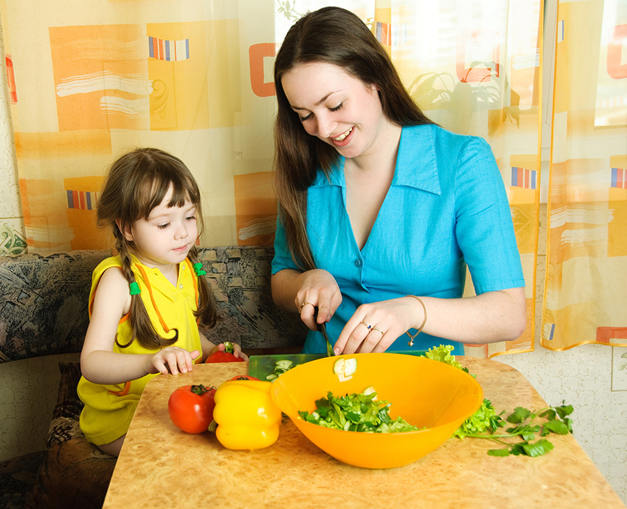 A woman cutting vegetables with a young girl