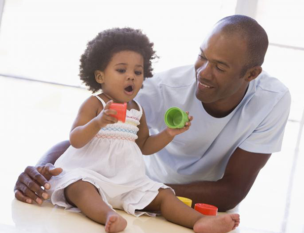 A man watches his daughter play with some plastic toys and smiles at her. 