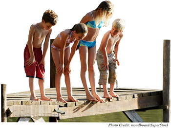 4 children (two girls and two boys) aged 6 to 11 standing on the edge of a dock in their bathing suits.