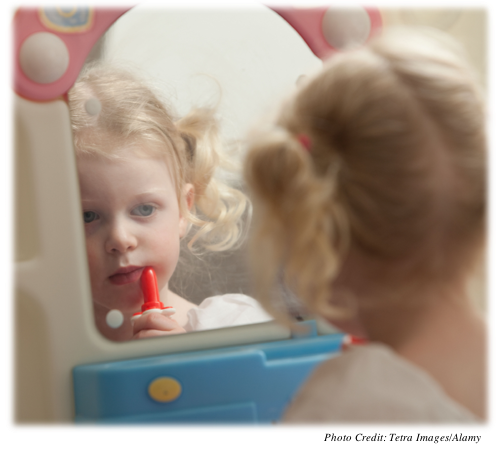 A toddler playing with lipstick while looking in her own reflection.