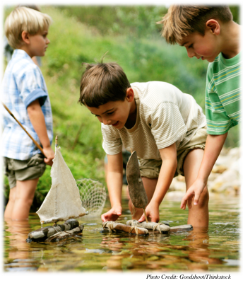 Three young boys playing in a stream building boats out of sticks