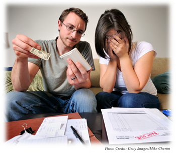 A young couple going over their bills, one of which says “past due.”  They both look worried, and the wife is hiding her face in her hands.