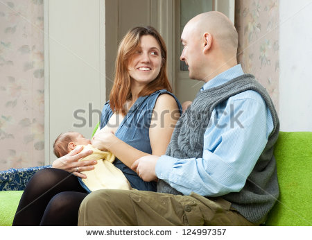 Color image of a man and woman sitting together while the woman breast-feeds her baby.