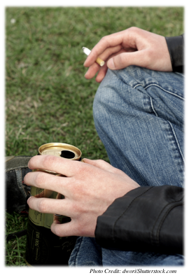 Teenage boy sitting on the ground holding a cigarette and a can of beer