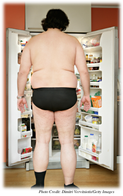 An overweight man standing in front of a very full open refrigerator