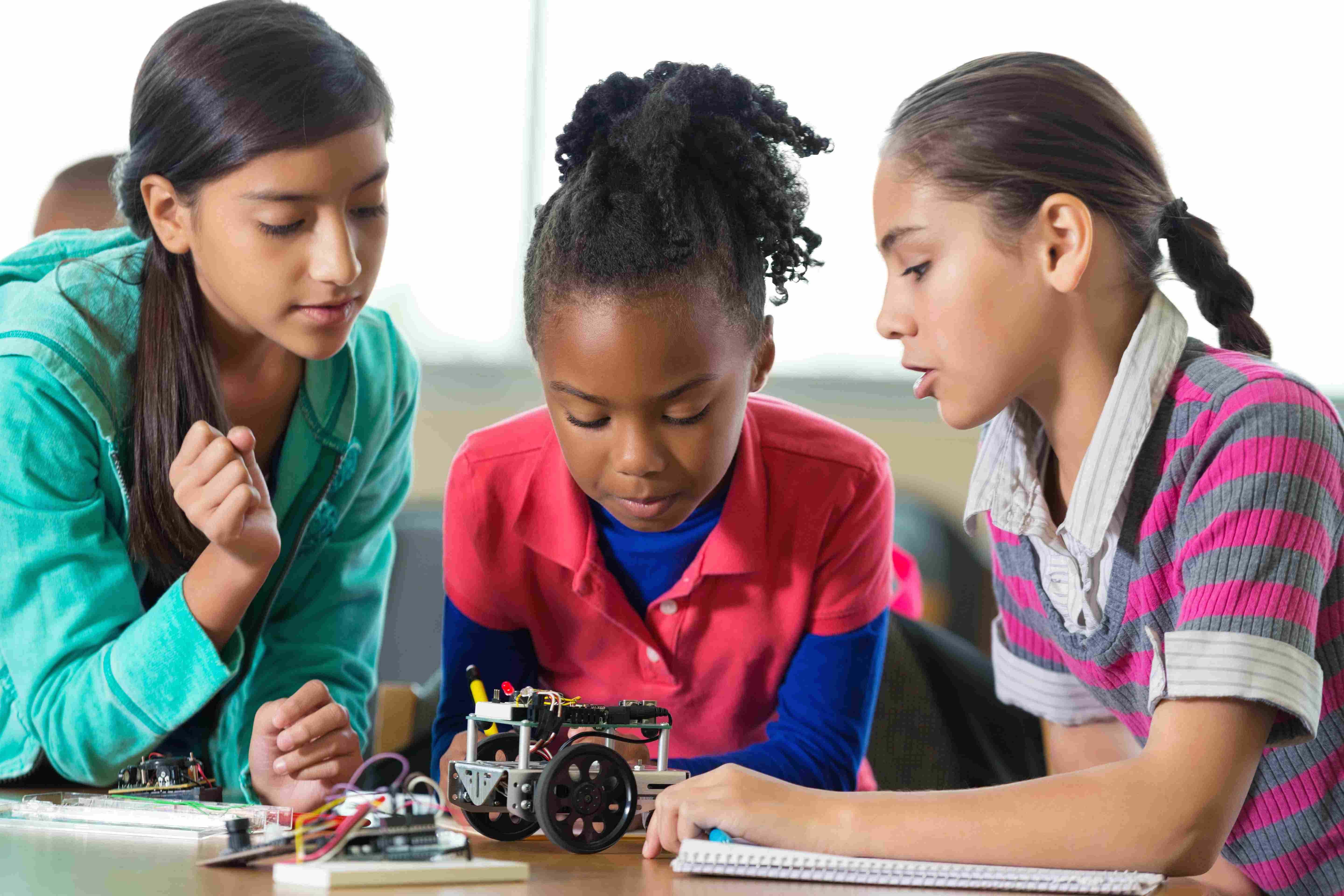 Three girls are studying a small mechanical vehicle