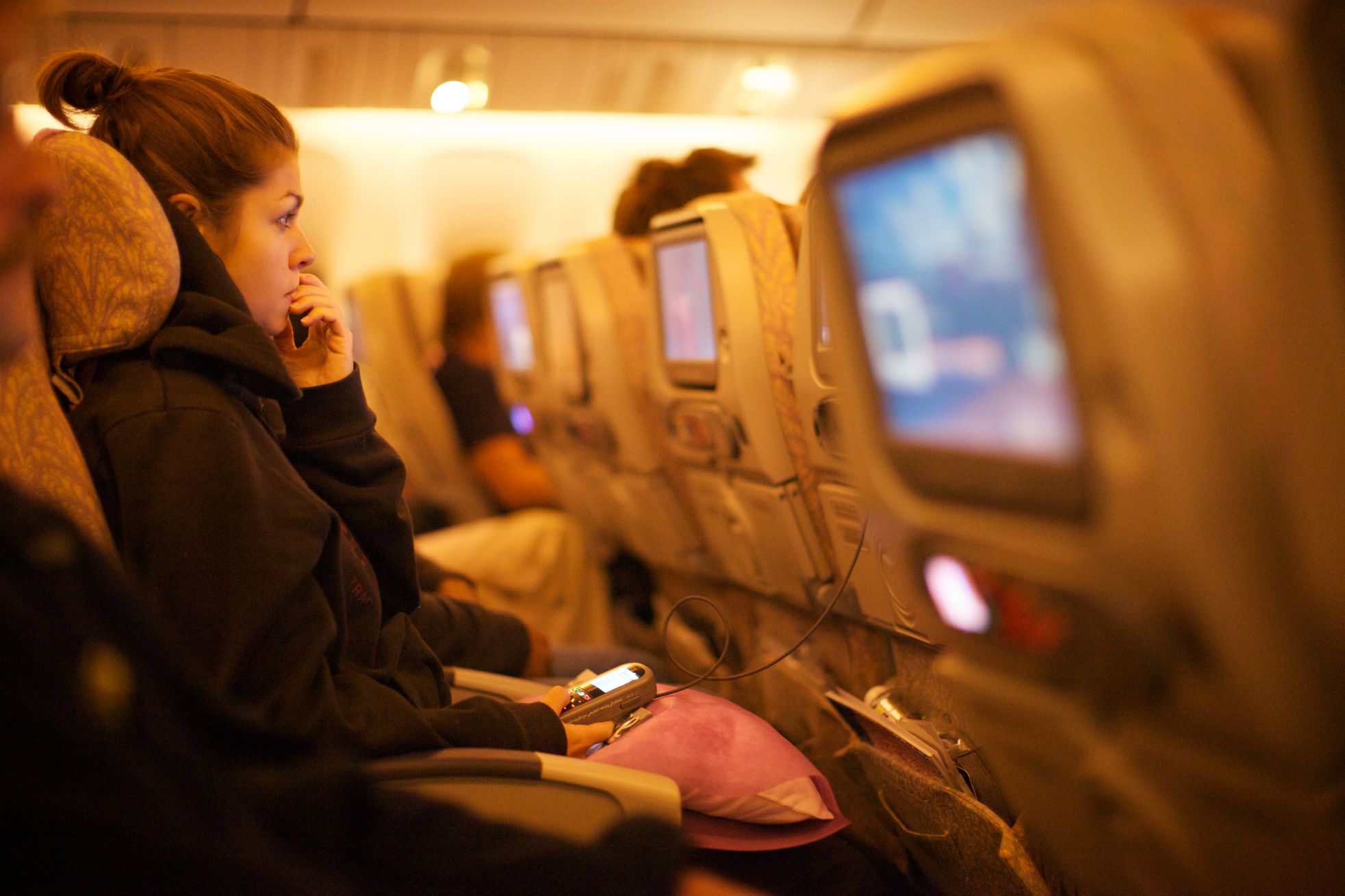 A woman on a flight looks stressed as she watches a video on a screen mounted in a headrest. 