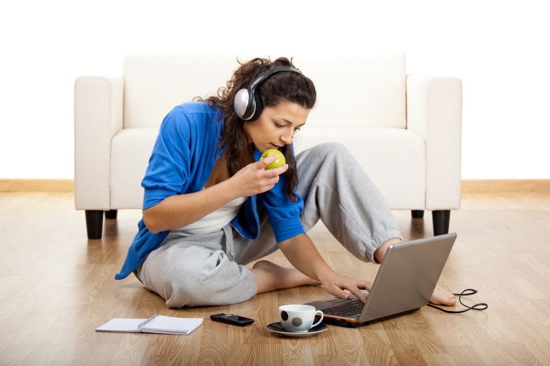 A woman multitasking while using a laptop, eating , and listening to music through headphones.