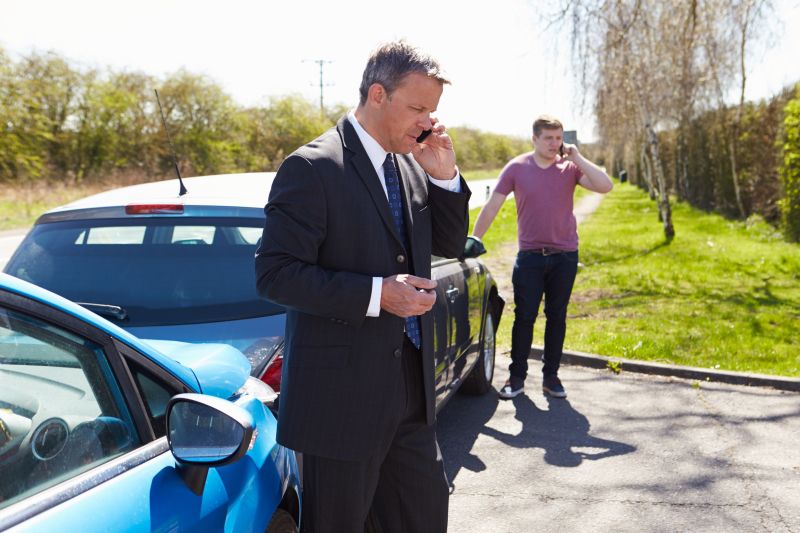 Photo shows two men talking on their mobile phones in front of two cars that hit one another, perhaps due to multitasking.