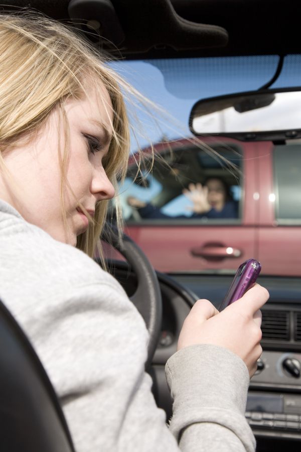 The photo shows a woman looking at her mobile phone while driving and she does not notice a car in front of her. This picture signifies intentional blindness caused by multitasking.