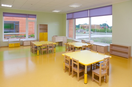 a classroom with wooden tables, wooden chairs, and an open wooden floor.  There is nothing on the walls or ceiling.