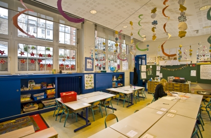 a classroom with long white tables and stools.  There are curly pieces of paper hanging from the ceiling and one wall is painted blue.