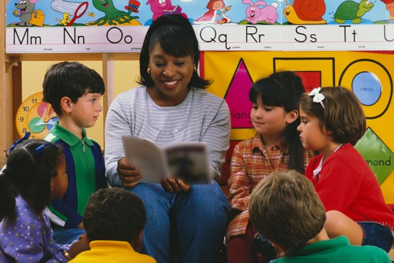 A teacher reads a book and teaches science to kindergarten students in a decorated classroom. 