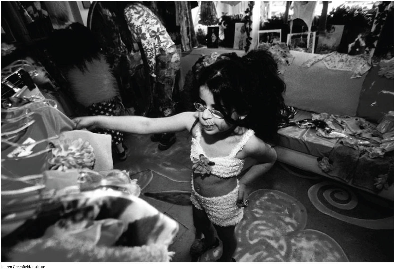 A black and white photo shows a small girl choosing a dress from a wardrobe.