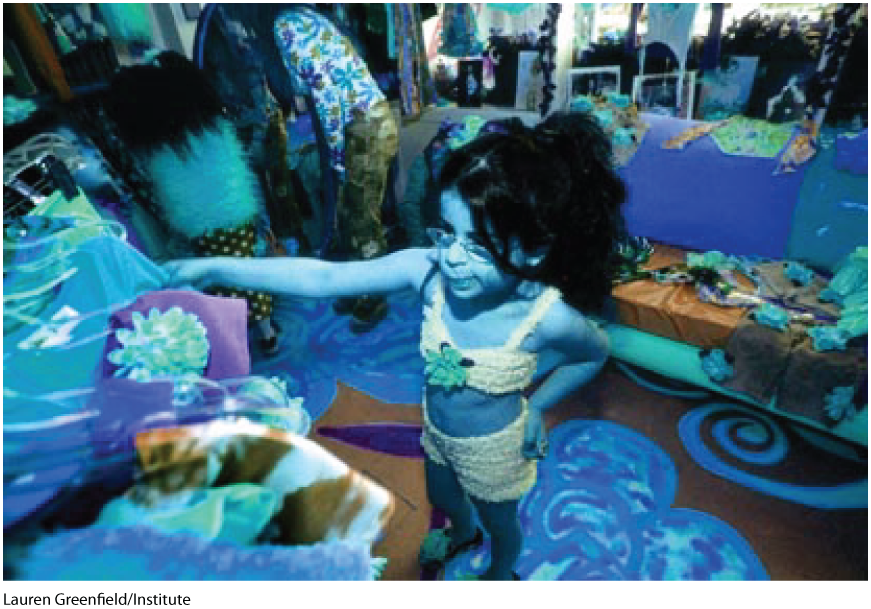 A blue tinted photo shows a small girl choosing a dress from a wardrobe.