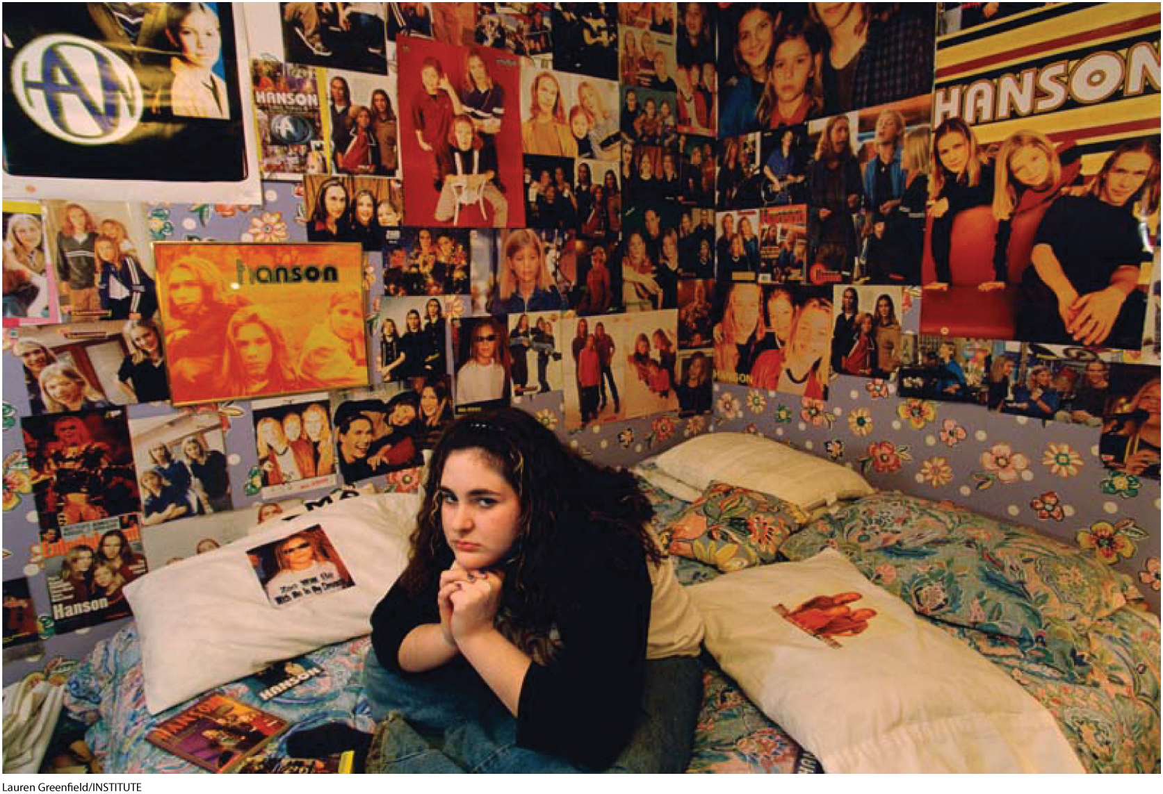 A photo shows a teenage girl sitting in her bedroom; the room’s walls are covered with posters of various music bands.