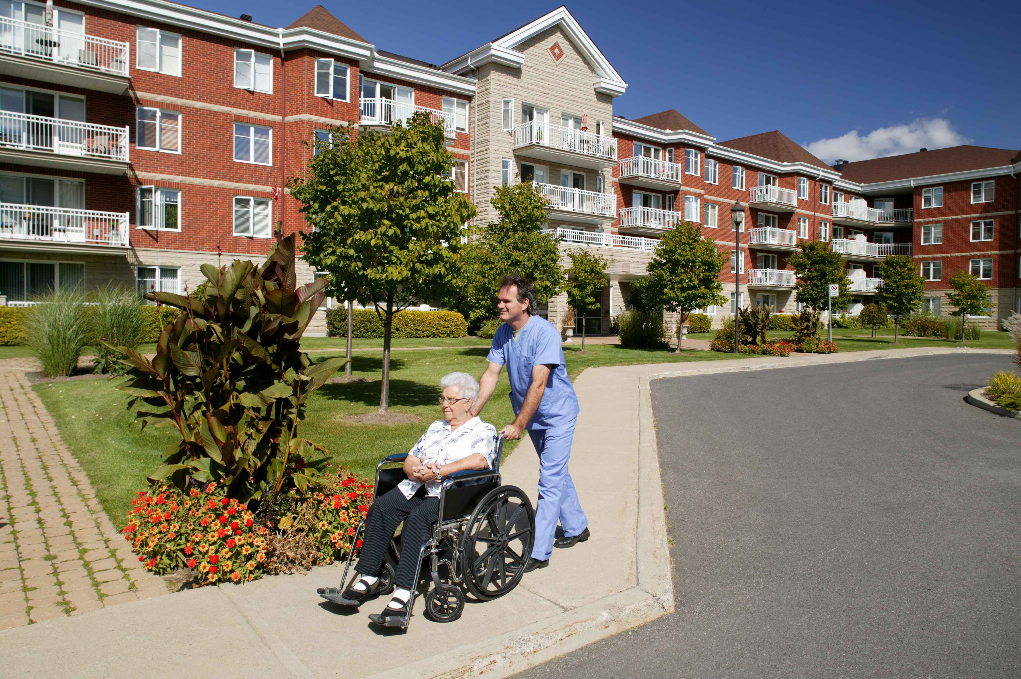 A male nurse drives a wheelchair with a senior person outdoors.