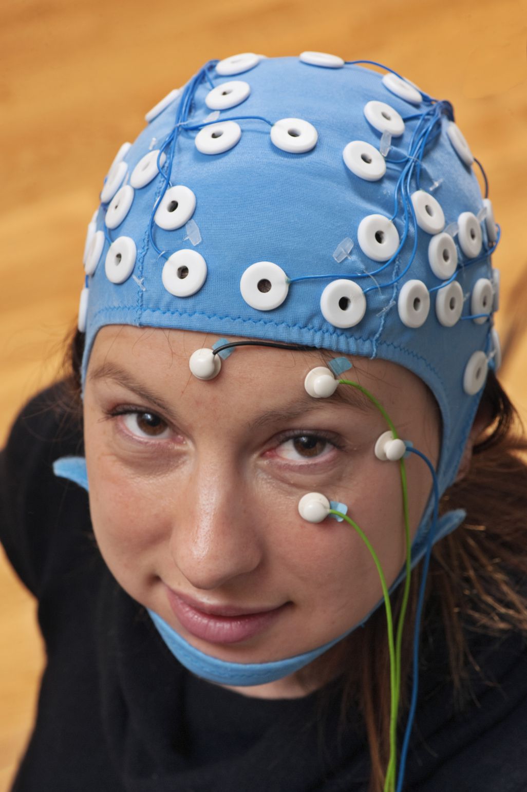 Woman wearing a cap fitted with a network of electrodes for use in electroencephalography (EEG) studies to measure electric current flows within the neurons of different parts of the brain. Photographed at the Oxford Centre for Human Brain Activity, UK.