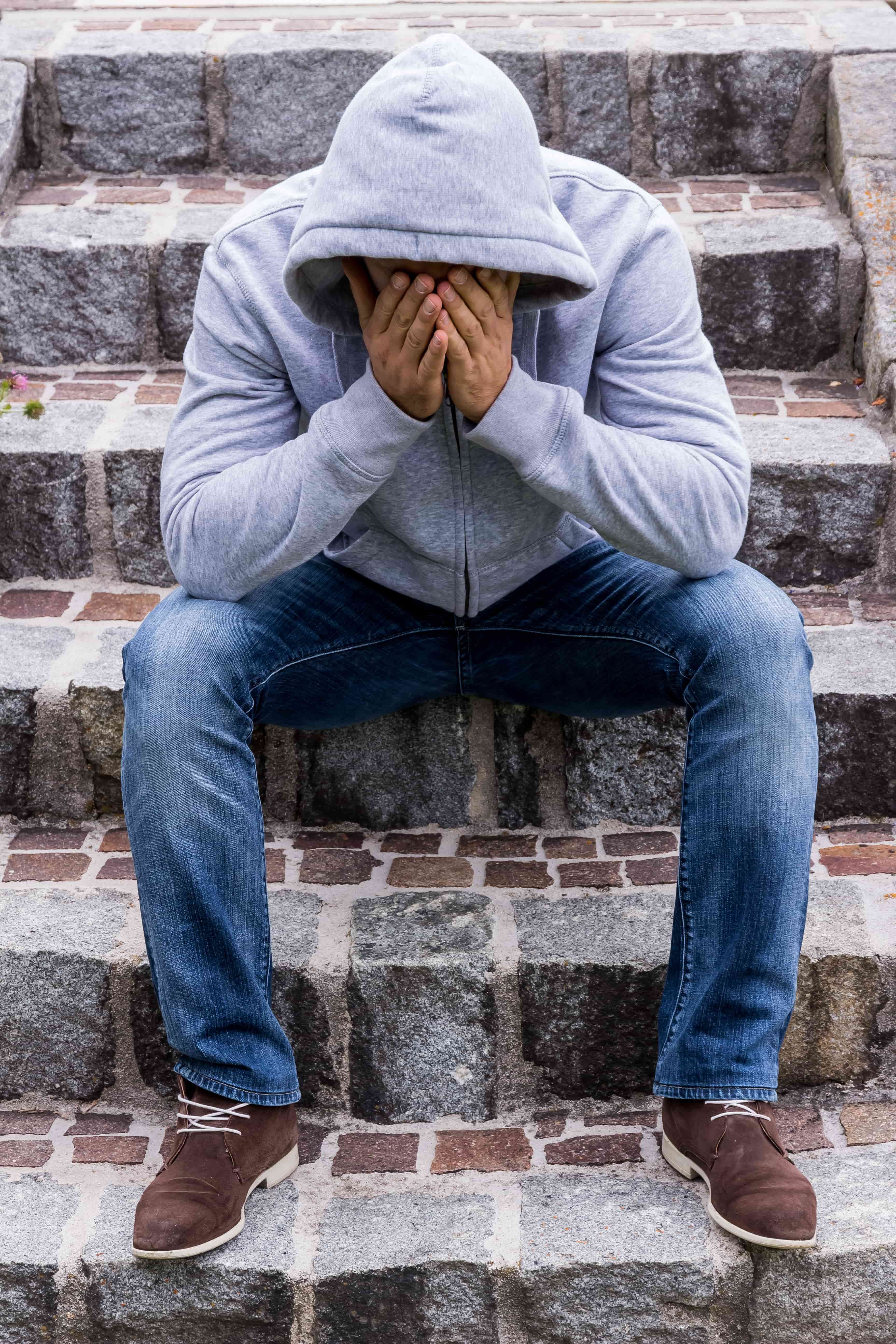 Man sitting on steps and covering his face with hands.