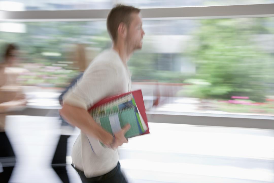 Blurred university student running in corridor with textbooks