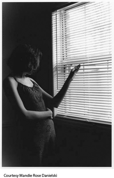 Black-and-white photo of a woman peeking through window blinds