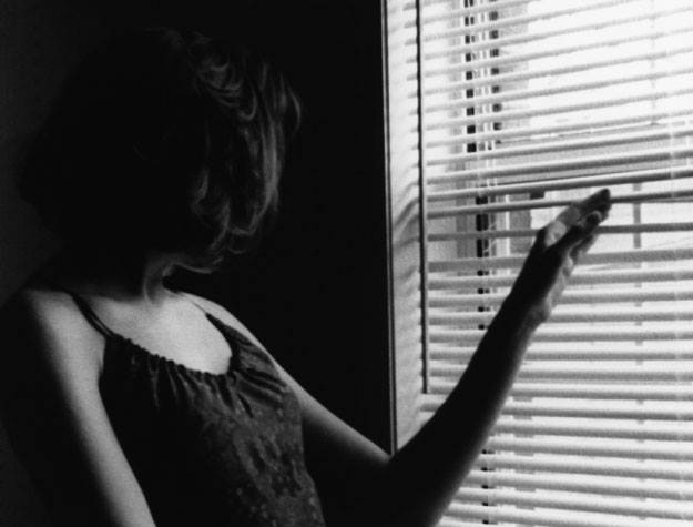 Close-up of a woman peeking through window blinds