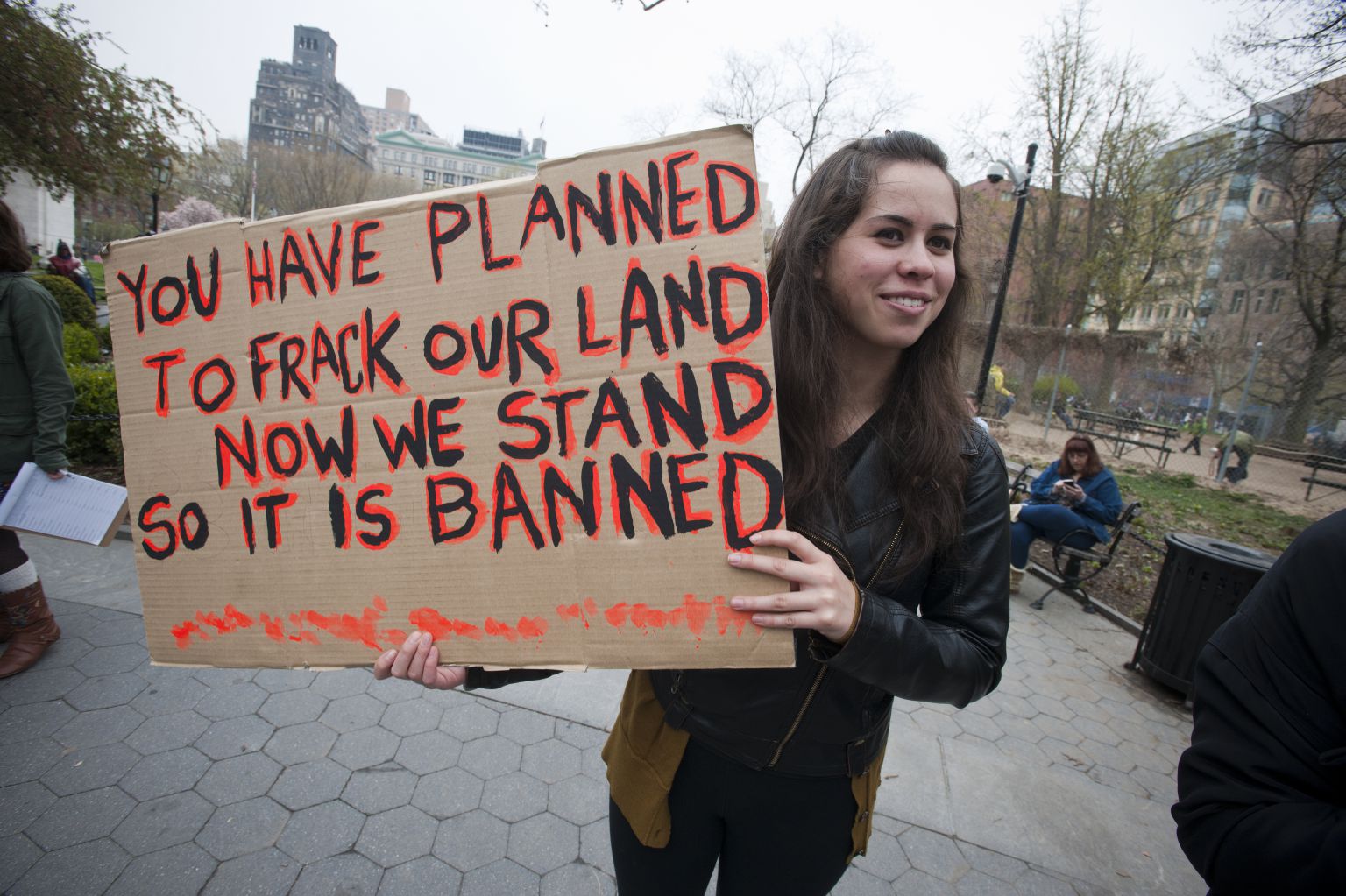 A teenage girl at a protest holds a sign reading "You have planned to frack our land, now we stand so it is banned."