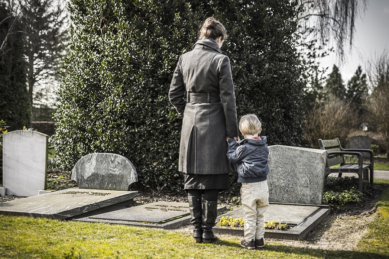 A mother and her son stand at a gravestone.