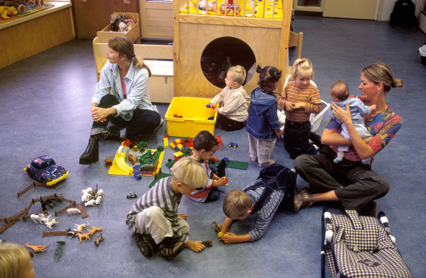 Toddlers and infants play with toys and their teachers at a child care center.