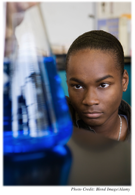 A teenage boy studying a beaker filled with blue liquid.