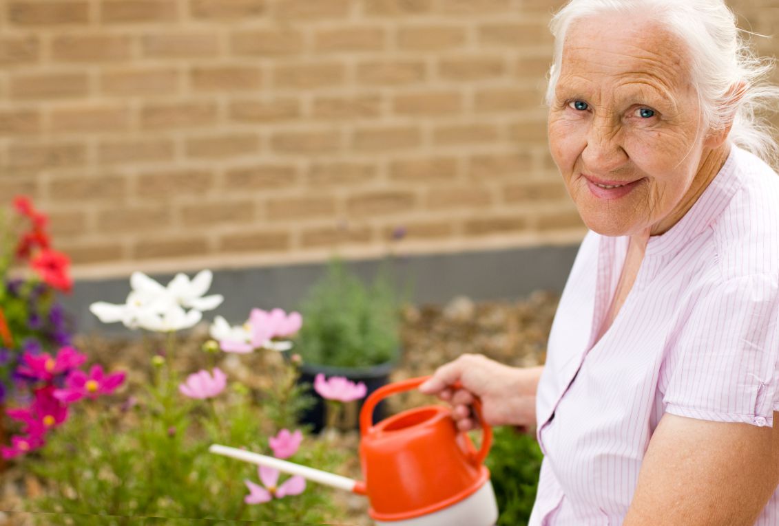 A smiling elderly lady watering flowers.