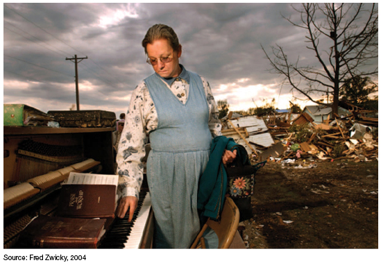 Figure. Photograph. A sample photograph in which a woman wistfully touches the keys of a piano surrounded by debris from apparent storm damage. The woman is holding a jacket. A book of hymns sits atop the piano. A photograph can accompany text to add a visual dimension to the written text, or it can be the subject of a piece of analytical writing. This photograph can be analyzed in a number of ways, focusing on the woman's expression, her action, what she is holding, the debris in the background, the hymnal, the telephone pole, and so on. (The source is Fred Zwicky.)