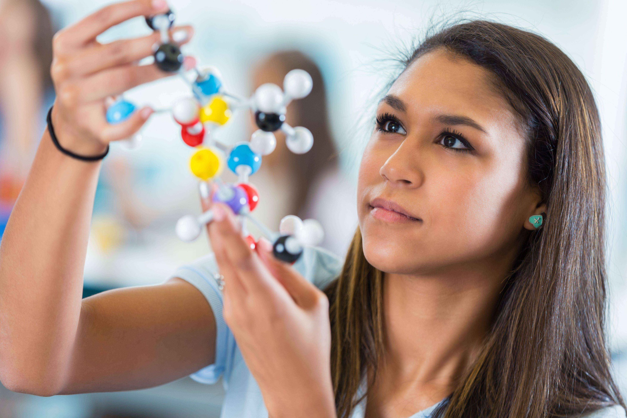 A teenage girl is holding a model of a chemical compound. She is 12 years of age or older