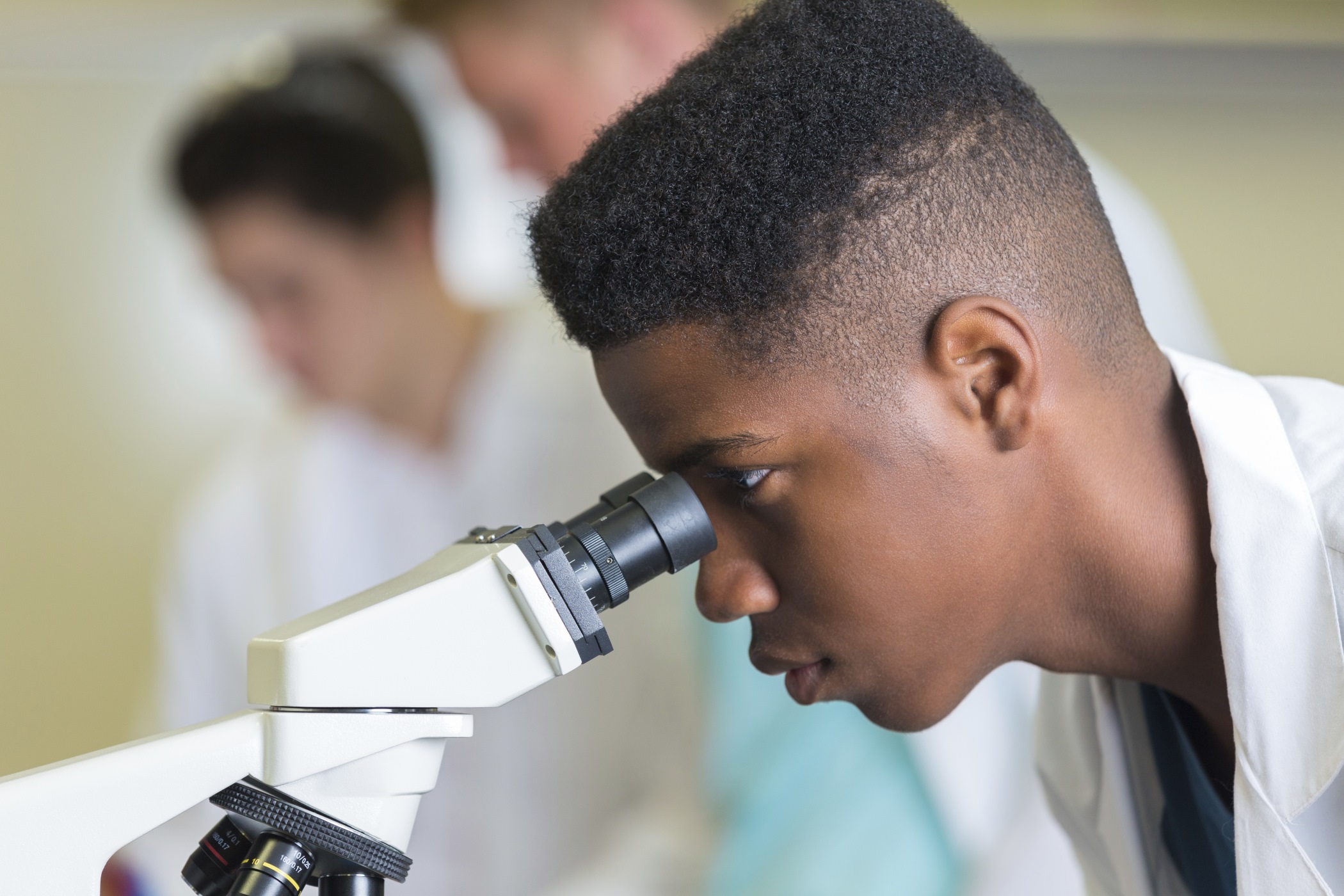 a teenage boy looking through a microscope who is 12 years old or older