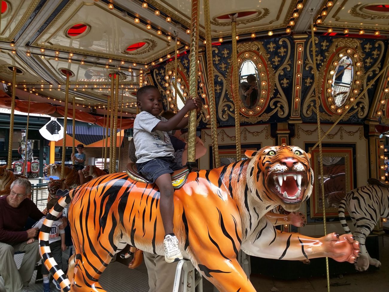There are two images of the same scene.  The scene is a boy on a carousel riding a fake tiger. 