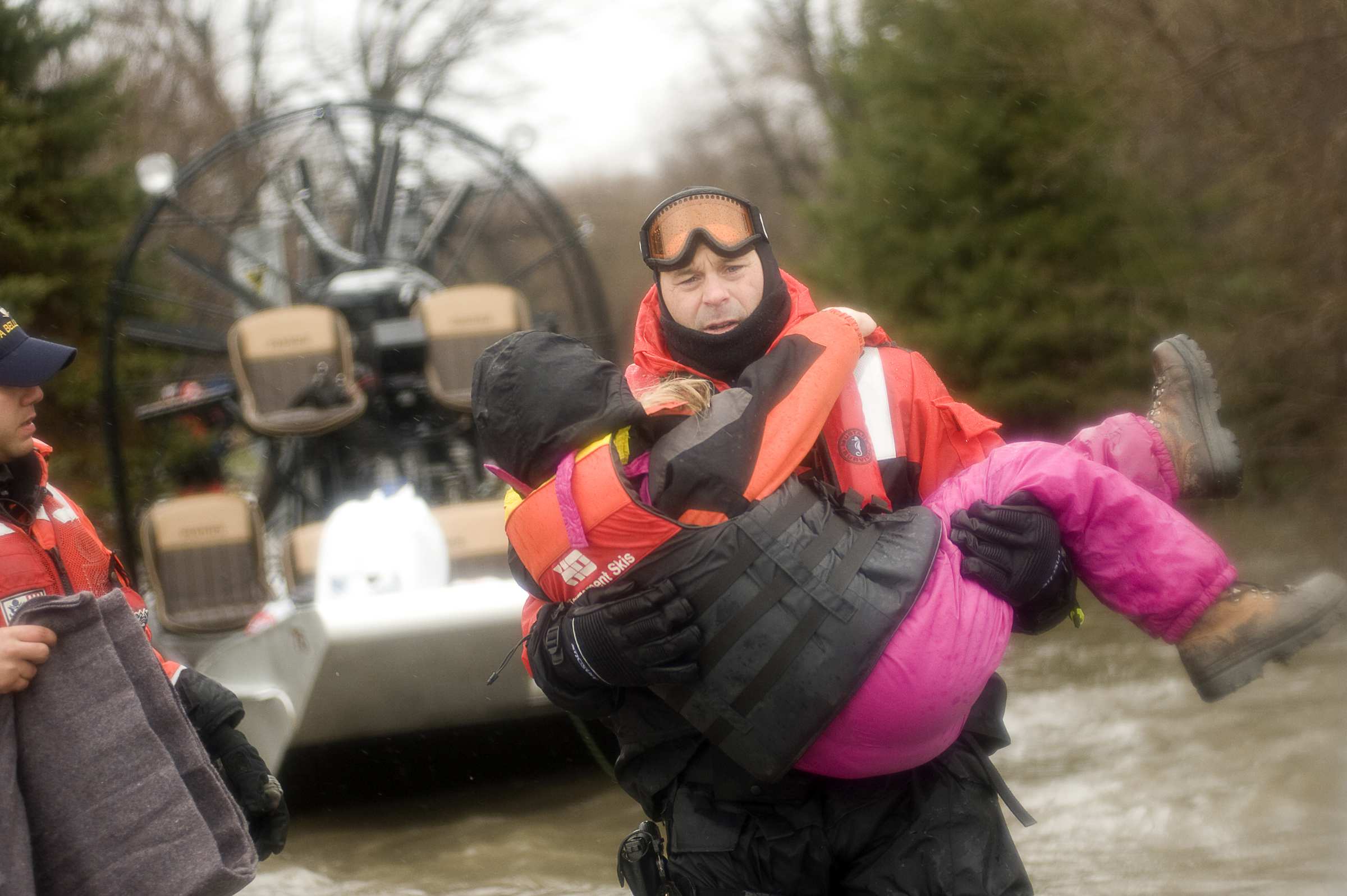 A rescue team carries a girl away from a river.